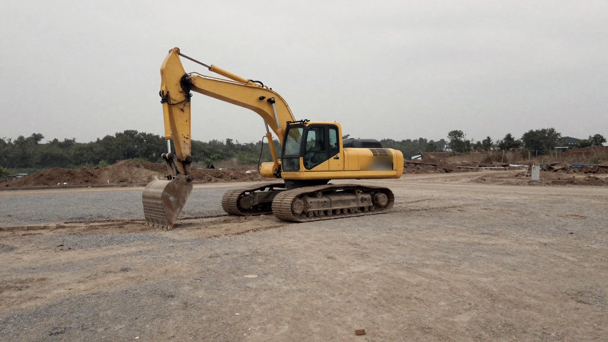 A tracked excavator parked on a graded dirt job site under an overcast Fraser Valley sky
